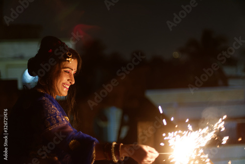 Young and beautiful Indian Bengali/gujarati/rajasthani woman in Indian traditional dress is celebrating Diwali with fire crackers on rooftop in darkness. Indian lifestyle and Diwali celebration