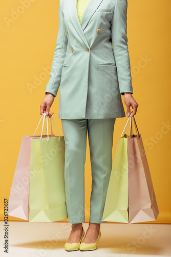 african american girl in suit holding shopping bags on yellow