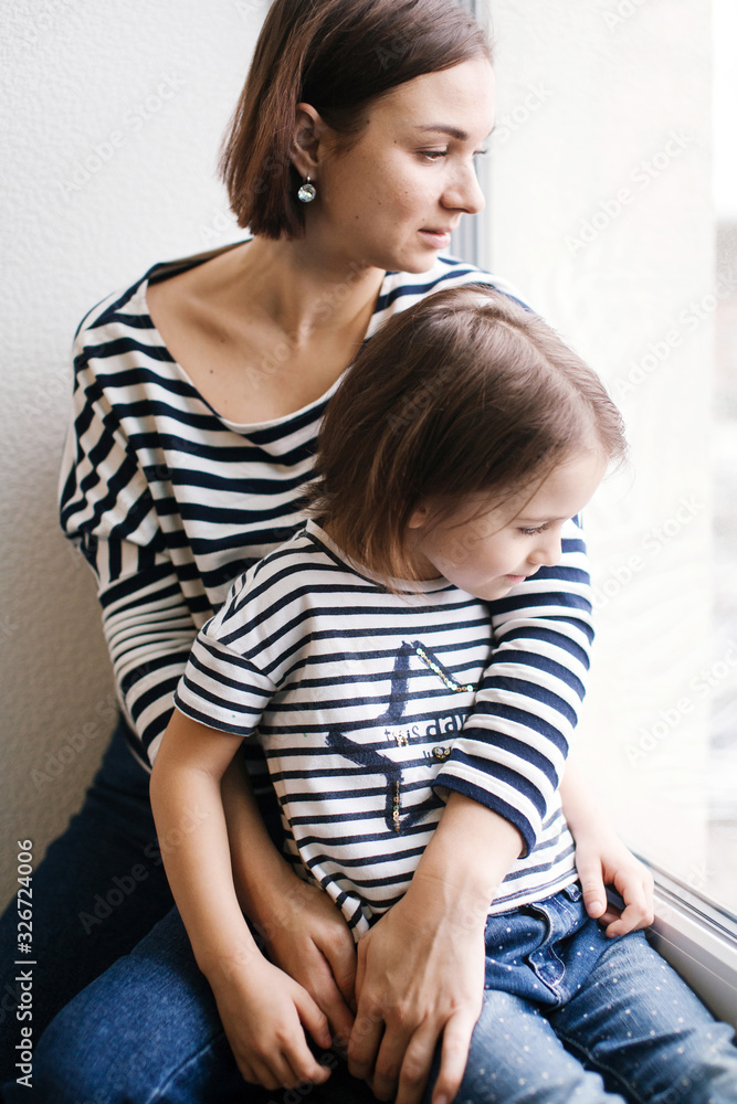 Calm young mother with adorable girl child at home near window, close-up portrait Calm young mother with adorable girl child at home near window, close-up portrait