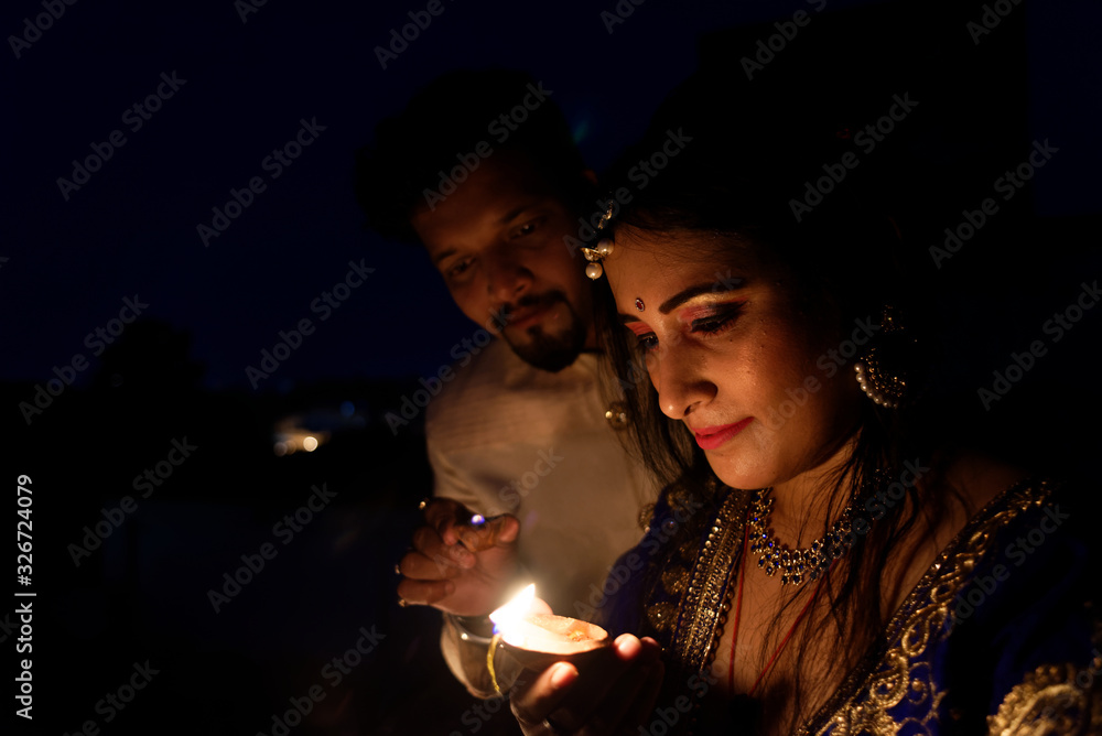 Young and beautiful Indian Gujarati couple in Indian traditional dress lightening Diwali diya/lamps sitting on the terrace in darkness on Diwali evening. Indian lifestyle and Diwali celebration Young and beautiful Indian Gujarati couple in Indian traditional dress lightening Diwali diya/lamps sitting on the terrace in darkness on Diwali evening. Indian lifestyle and Diwali celebration