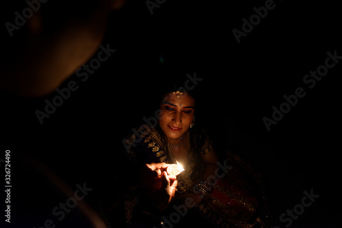 Beautiful Indian Gujarati couple in Indian traditional dress lightening Diwali diya/lamps sitting on the floor in darkness on Diwali evening. Indian lifestyle and Diwali celebration