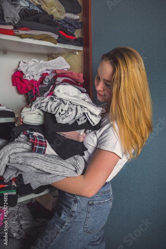 Fast fashion, the girl puts things in order in the closet. A bunch of colorful clothes. The concept of processing, second hand, eco, minimalism, consumption of goods. photo