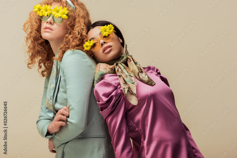 stylish african american girl and curly woman in sunglasses with flowers posing isolated on beige stylish african american girl and curly woman in sunglasses with flowers posing isolated on beige