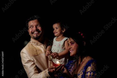 Young and beautiful Indian Gujarati father,mother and kid in traditional dress celebrating Diwali with diya/lamps on the terrace in darness on Diwali evening. Indian lifestyle and Diwali celebration