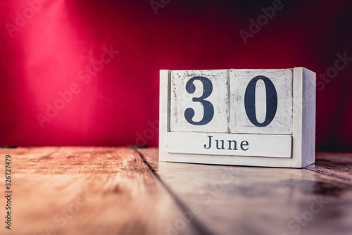 June 30th. Day 30 of month, calendar on business office table, workplace with vivid maroon red background. Summer time