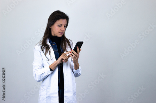 Portrait of attractive caucasian bussiness woman holding phone, reads whatsapp, isolated on gray background studio shot, in white coat uniform, dark air. Place for your text in copy space.