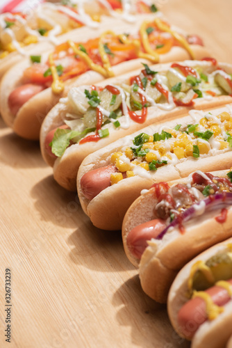 selective focus of fresh various delicious hot dogs with vegetables and sauces on wooden table