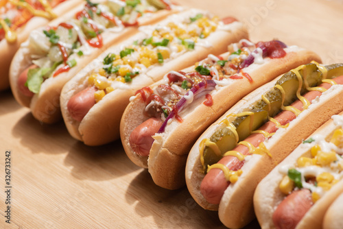 selective focus of fresh various delicious hot dogs with vegetables and sauces on wooden table