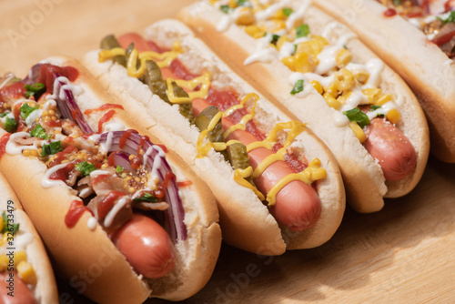 various delicious hot dogs with vegetables and sauces on wooden table