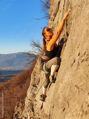 VERTICAL: Athletic woman wearing sunglasses climbs up a challenging rocky wall. © helivideo
