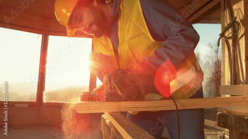 CLOSE UP: Golden sunbeams shine through the window as worker sands a long board. photo