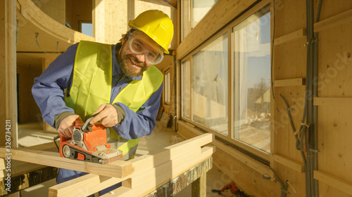 PORTRAIT: Smiling builder working on a prefabricated house buffs a wooden beam.