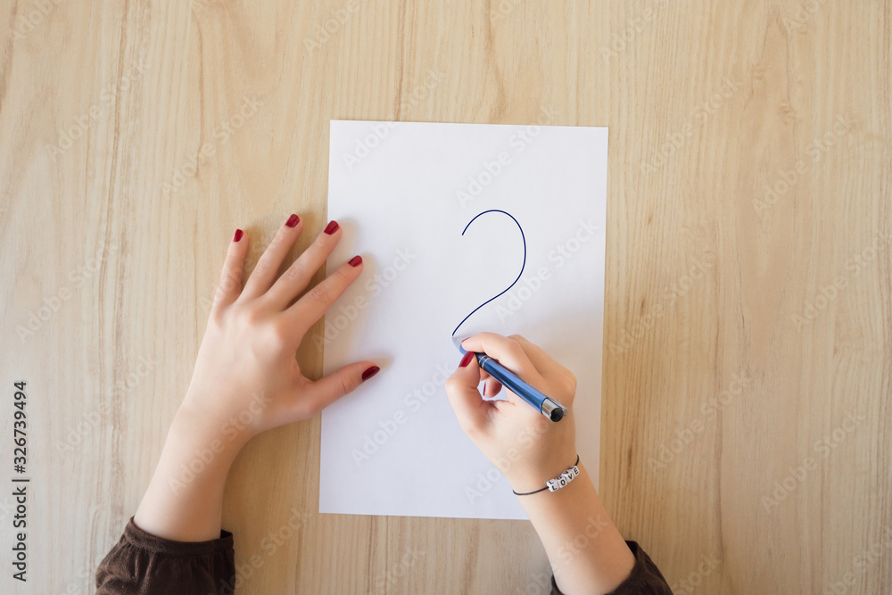 A woman draws a question mark on a blank sheet of paper. View from above. Flat lay A woman draws a question mark on a blank sheet of paper. View from above. Flat lay