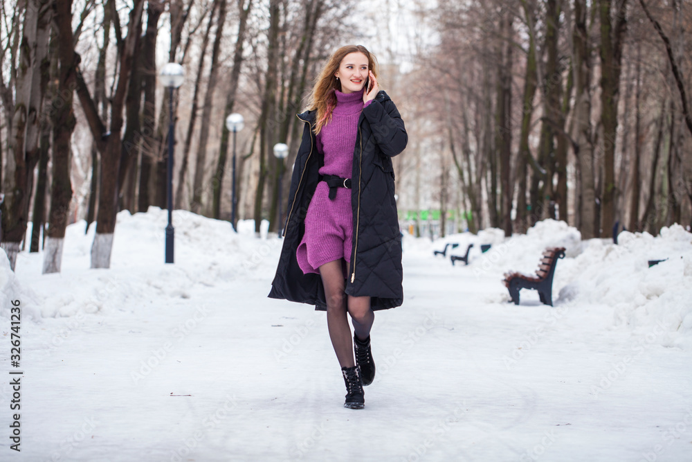 Full-length portrait of a young woman in black long down jacket posing in winter park Full-length portrait of a young woman in black long down jacket posing in winter park