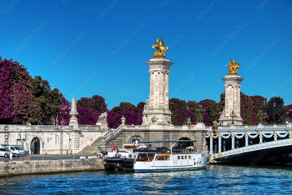 Pleasure boats docked on the Seine river next to the Alexander III Bridge, one of the most beautiful bridges that cross the Seine river, in Paris, France.