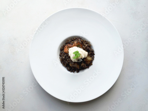 Top view black rice Paella in white plate with aioli sauce on top on white background