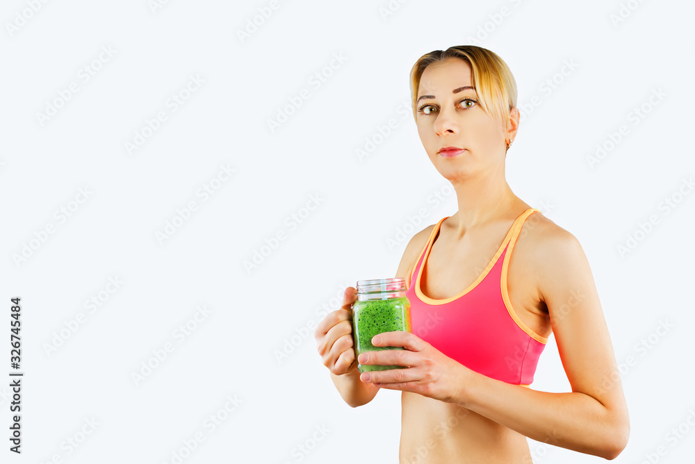 Sport blond girl in tracksuit for sport exercises with glass of green smoothie Sport blond girl in tracksuit for sport exercises with glass of green smoothie