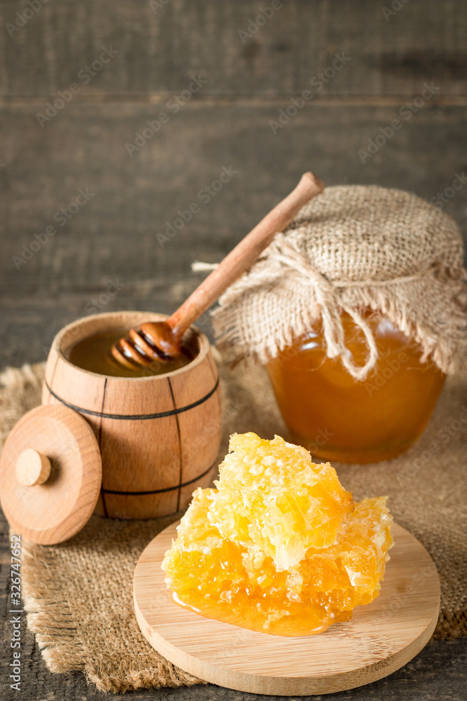 Fototapeta premium Honey dripping from a wooden honey dipper in a jar on wooden grey rustic background