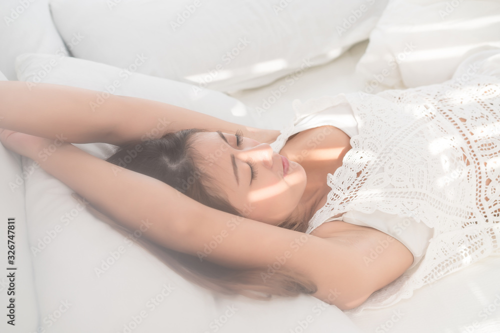 Obraz premium Portrait of beautiful Asian woman with attractive smile enjoy fresh soft bedding linen mattress in white bed room modern apartment. Cute asia girl sleep resting, good night sleep concept.