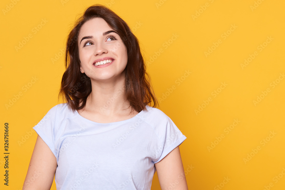 Obraz premium Close up portrait of happy brunette woman having idea and looking up with charming smile poising isolated over yellow background, adorale lady dresses casual outfit. Copy space for advertisment.