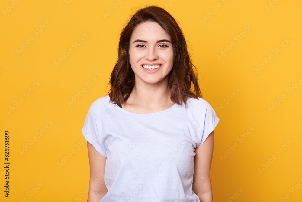 Caucasian woman posing isolated over yellow background, woman with charming smile looking happy directly at camera, adorable girl with dark hair, having good news, expresses happyness. People emotions Caucasian woman posing isolated over yellow background, woman with charming smile looking happy directly at camera, adorable girl with dark hair, having good news, expresses happyness. People emotions