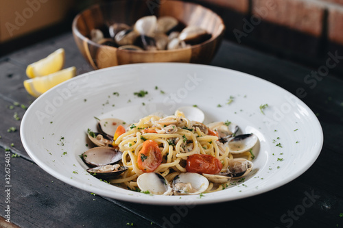 Pasta with clams on white plate on black background. Mediterranean delicacy food. Flat lay. Top view