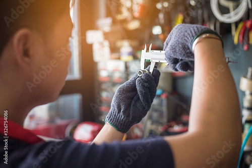 Mechanic man using a Vernier caliper to measure the object or engine part at motorcycle shop , selective focus photo