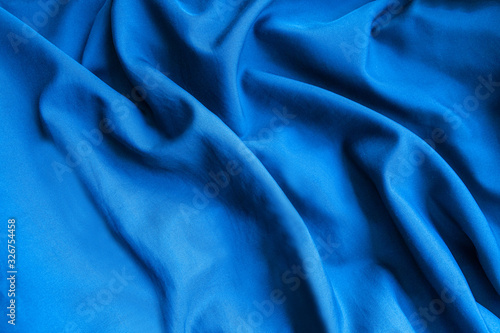 Blue satin fabric. Silk textile background. Wavy folds of material.