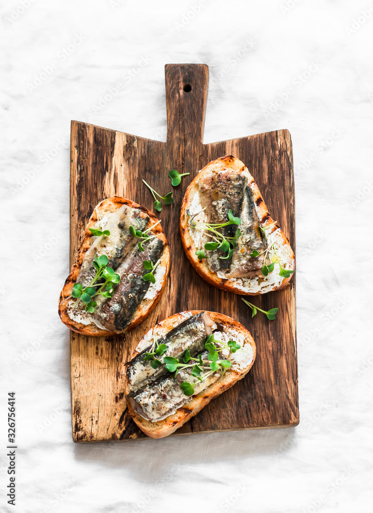 Grilled bread sardines micro greens sandwiches on a rustic cutting board on a light background, top view