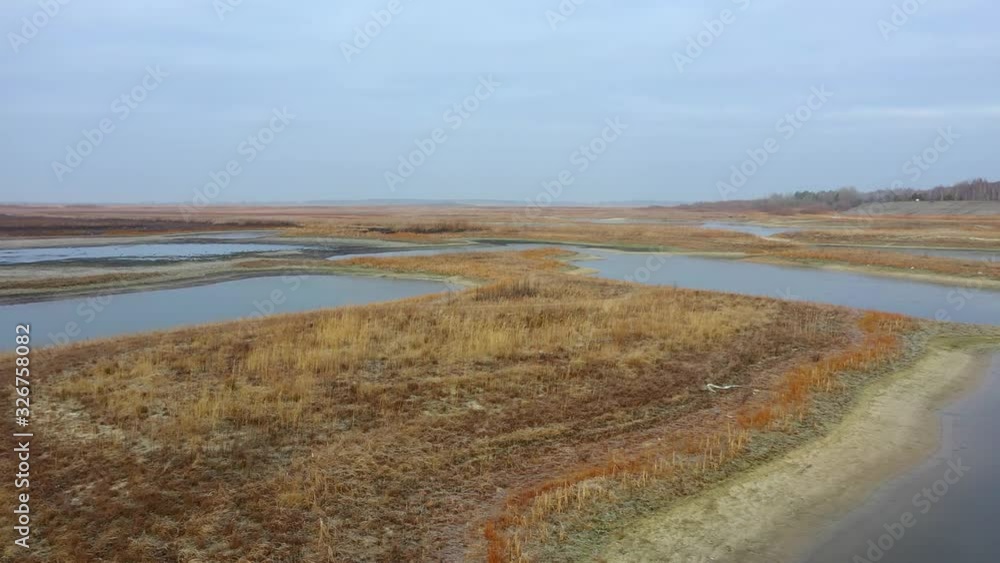A dry lake with indentations filled with water. Field flooded with water. Dry grass and fresh foliage, puddle and land, water-filled growing green grass and trees. Nature concept A dry lake with indentations filled with water. Field flooded with water. Dry grass and fresh foliage, puddle and land, water-filled growing green grass and trees. Nature concept