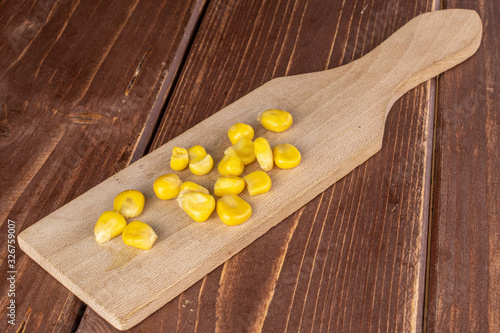 Lot of pieces of canned yellow corn on wooden cutting board on brown wood