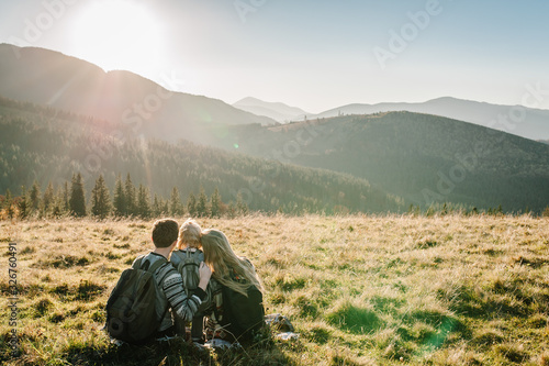Happy Hipster family: mom, dad, daughter with backpack enjoying sunset on peak of foggy mountain. Tourists traveler on background view mockup. Hikers looking sunlight in trip in country Europa. © Serhii