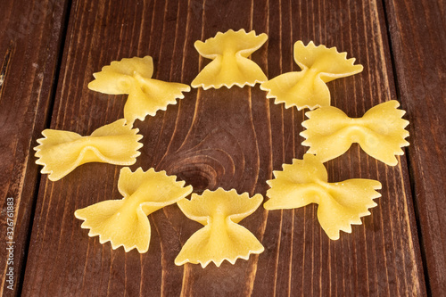 Group of eight whole yellow pasta farfalle on brown wood