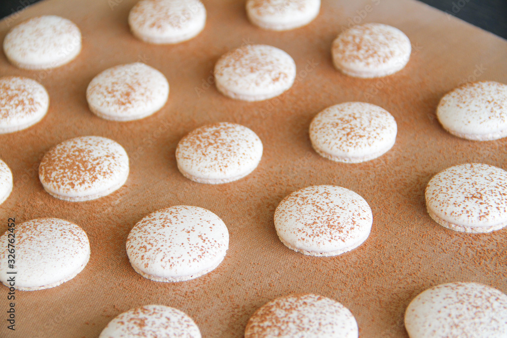 French dessert macaron. The photo of making macaron powdered with cocoa powder. Macaron in process, after baking, before filling. Macarons piped on a tray covered with a teflon sheet. Back view. French dessert macaron. The photo of making macaron powdered with cocoa powder. Macaron in process, after baking, before filling. Macarons piped on a tray covered with a teflon sheet. Back view.