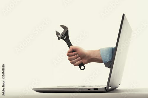 The human hand with black wrench stick out of a laptop screen. Concept of technical support.