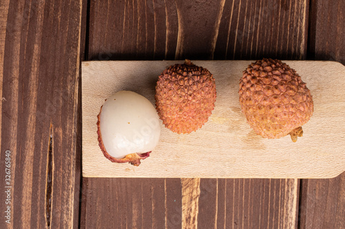 Group of three whole fresh lychee on wooden cutting board flatlay on brown wood