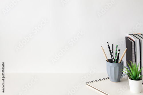 School desk against an empty white wall. Copy space. School supplies, books, succulent plant and notebook.