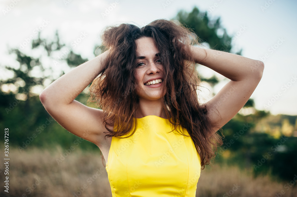 Girl with curly hair in a yellow dress smiles and has fun on the nature.