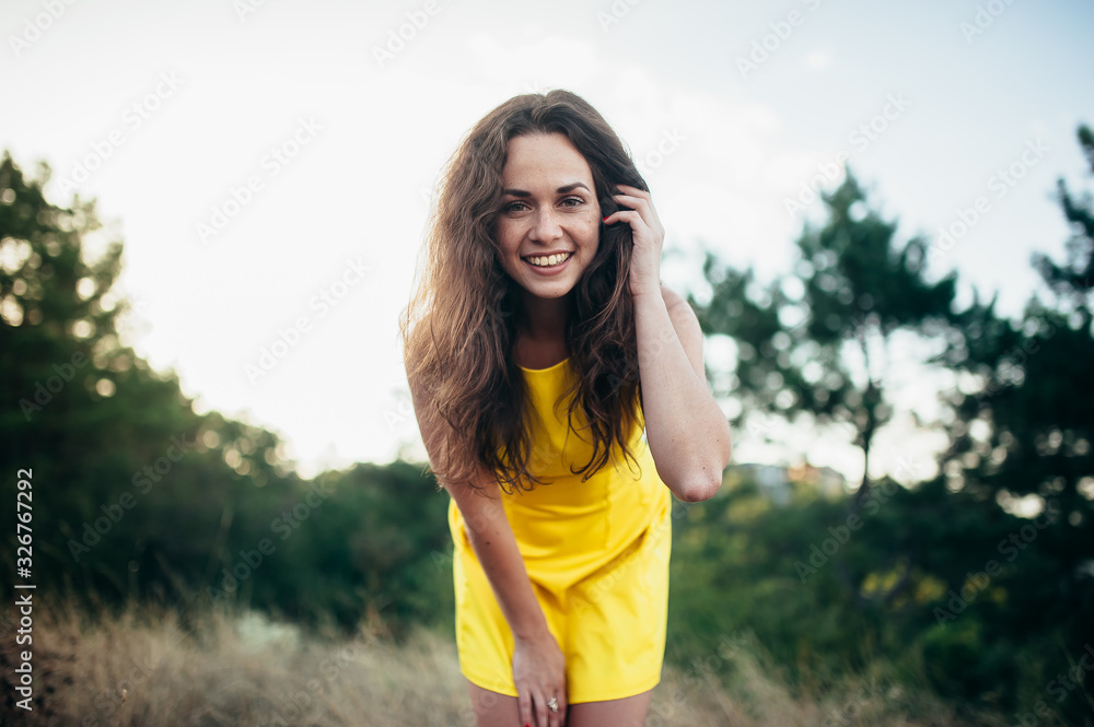Girl with curly hair in a yellow dress smiles and has fun on the nature.