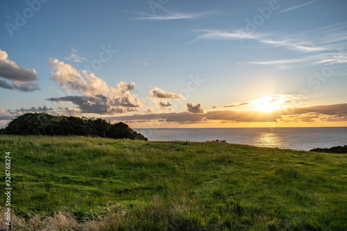 Golden sunse scene with green grass hills and ocean behind at Chiloe Island, Chile photo