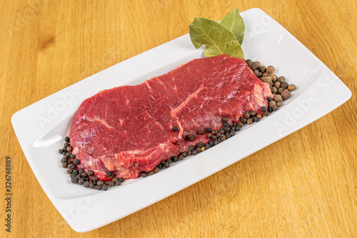Beautiful raw beef sirloin with spices on white rectangular ceramic plate on lacquered wood