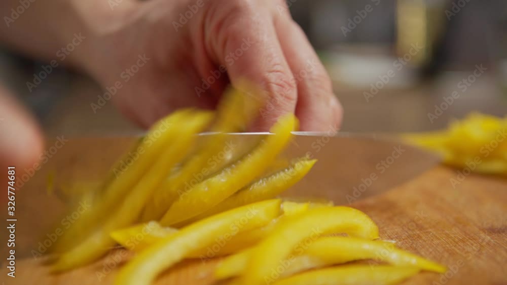 Zoom in closeup of hands of male chef cutting fresh ripe yellow bell pepper on wooden cutting board at kitchen table Zoom in closeup of hands of male chef cutting fresh ripe yellow bell pepper on wooden cutting board at kitchen table