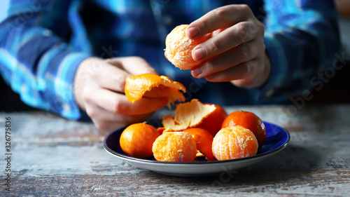 Men's hands are peeling mandarin. Tangerines in a plate. Mandarin peel.