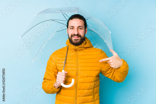 Young man wearing a long hair look holding an umbrella isolated person pointing by hand to a shirt copy space, proud and confident