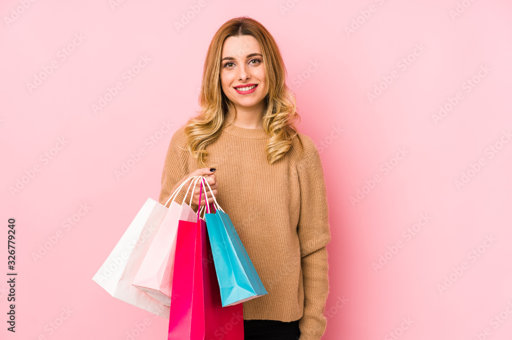 Young blonde woman holding shopping bags isolated happy, smiling and cheerful.