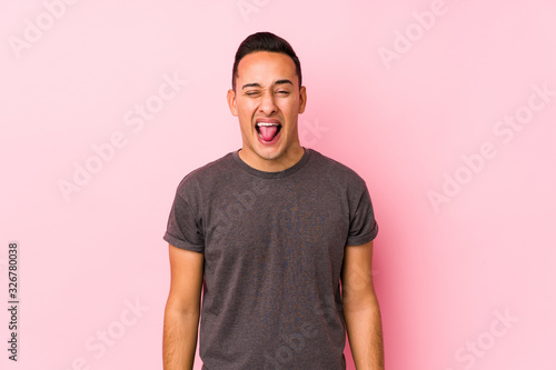 Yooung latin man posing in a pink backgroundfunny and friendly sticking out tongue.