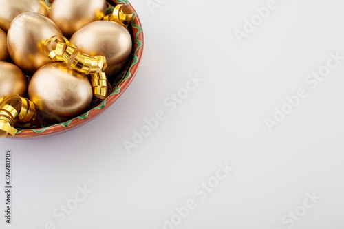 Golden eggs in a plate, on a white background, decorated with gold ribbons, next to the place for text, with copy space. The concept of Passover and the holiday symbol.
