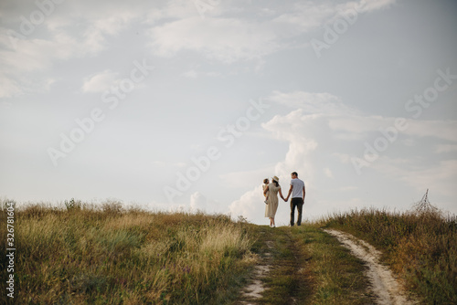 Family, mom, dad, daughter are walking on a hill in the field. Mom and daughter in yellow identical dresses. © malysheva