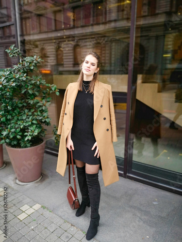 Fashion portrait of beautiful stylish woman with coat in the city. Holding purse in hands and has  a serious look. Photo taken in Belgrade, Serbia.