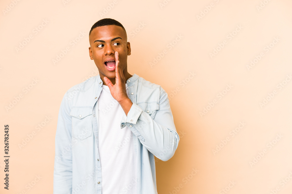 Young latin man isolated on beige background is saying a secret hot braking news and looking aside Young latin man isolated on beige background is saying a secret hot braking news and looking aside